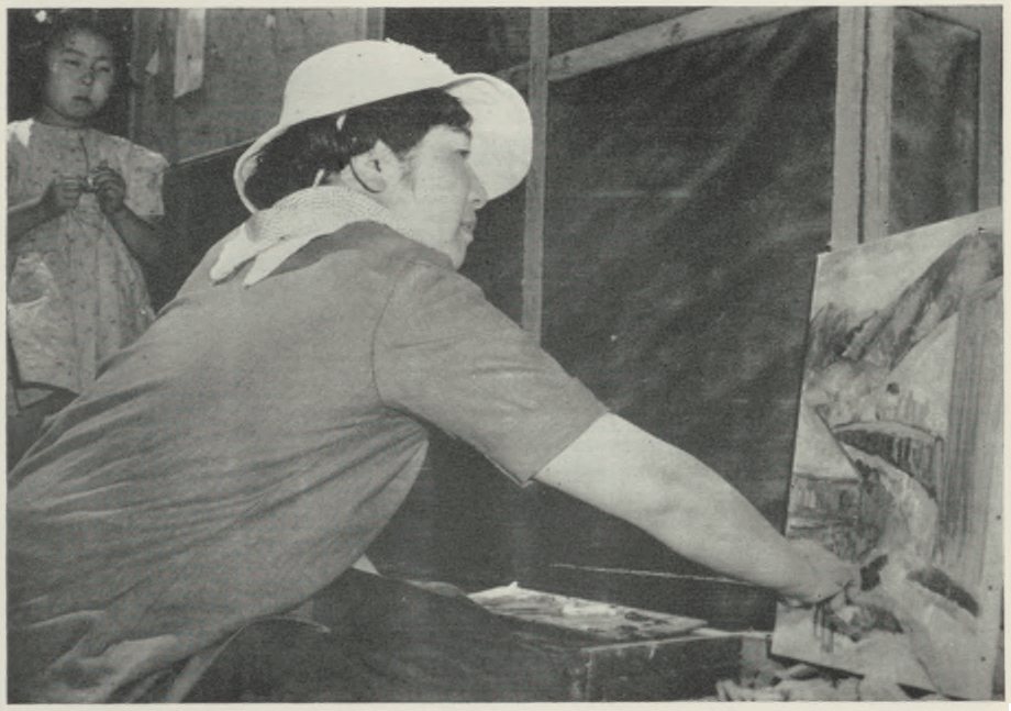 A black and white photograph of Hisako Hibi in the process of creating her painting entitled "Barrack 9"